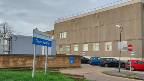 OWEN WARD/BBC Orsett Hospital. Picture taken of part of its exterior, which is grey. Cars are parked next to it and there is a sign saying "Orsett Hospital".