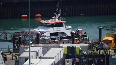 Getty Images People are offloaded from a boat at a port. 