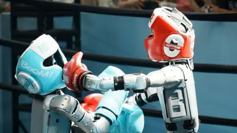 CFOTO/Future Publishing via Getty Images Two robots boxing in a ring. One has a light blue head protector with matching gloves, the other wears red.