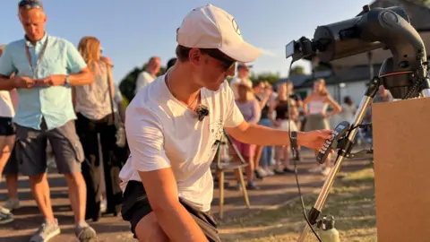 A man holding a large camera on a tripod as he adjusts it