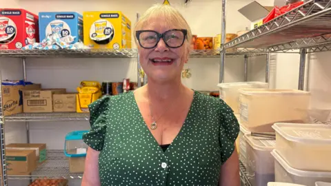 A woman wearing a green short sleeved dress with white spots on it smiles into the camera. 