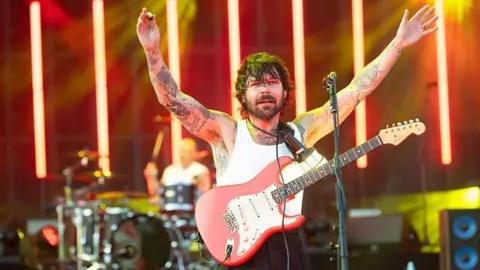 Getty Images Simon Neill of Biffy Clyro onstage. He has a guitar strapped on and his hands in the air.