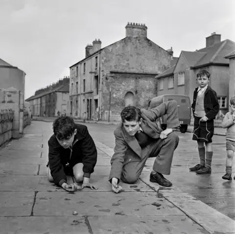 Bert Hardy/Getty Images Boys dressed in blazers playing with marbles on a residential street