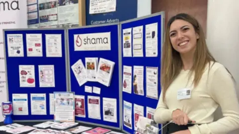 A woman wearing a white jumper stood next to a fundraising table