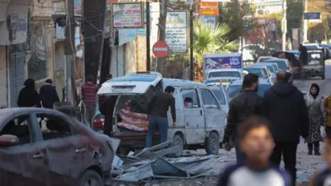 Reuters People walk past a damaged site in Aleppo after air strikes by Russian forces. 