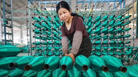 A woman stacks rolls of bright green fishing nets on a production line at factory