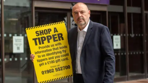 Wolverhampton City Council Councillor Craig Collingswood stands holding an anti fly-tipping sign