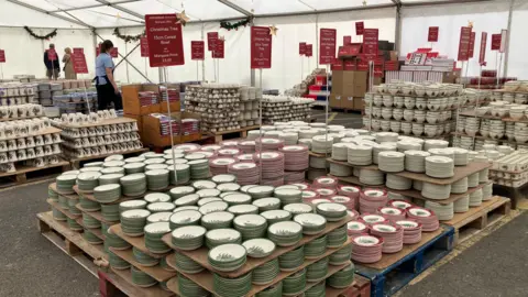 Layers of red and green ceramics are spread across the ground inside a large marquee