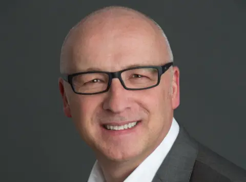 Ferguson Marine A shaven-headed bespectacled man in a grey suit and white shirt