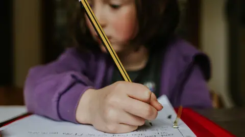 Getty Images Focus on a pencil that a little girl holds as she does homework - stock photo