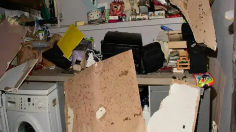 PA Wooden parts of the roof are scattered around the room in pieces against a shelf of trinkets and photos. 
