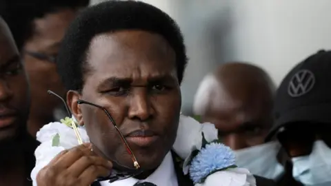 Venancio Mondlane (centre) wearing a black suit and a flower necklace walks with people upon his arrival at the Maputo International Airport in Maputo