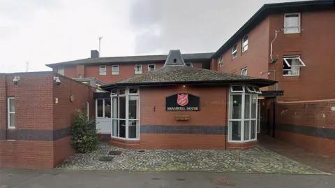 Google External view of The Salvation Army's Bramwell House hostel. It is a red brick building with the charity's sign in its signature black and red colours.