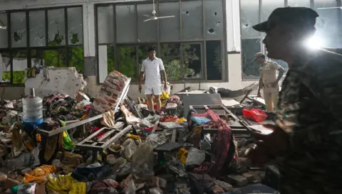 Hindustan Times via Getty Images People stand amid a chaotic scene of debris within the doctors' mess hall after the crash. It is clearly dark outside, meaning it is several hours since the incident