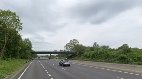 A Google street view screenshot of a four-lane motorway with trees on either side.