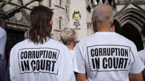 PA Media Two people with their backs to the camera. Their T-shirts read: "Corruption in Court".