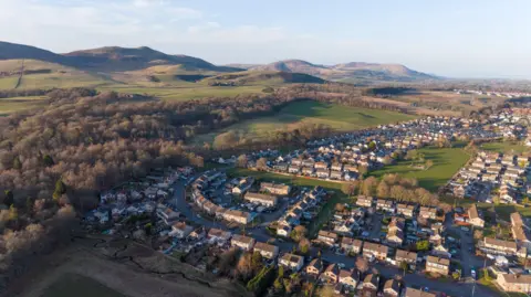 Getty Images An aerial view of Penicuik. There are rows of houses and a low, wooded hill. There are higher hills on the horizon.