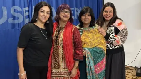 Wolverhampton Literature Festival A group of four women, two dressed in south asian clothing, stood in front of a stage smiling at the camera