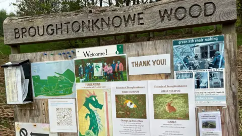 A wooden noticeboard with lots of posters and maps
