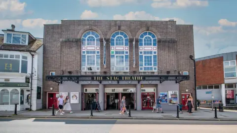 A theatre building. It is brick with pretty, curved windows. 