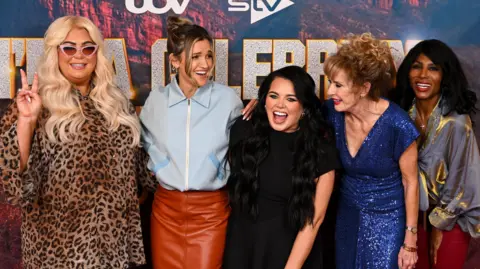 Getty Images Gemma Collins, Ashley Roberts, Scarlett Moffatt, Beverley Callard and Sinitta standing in a row with their arms around each other and smiling at the press launch in front of the I'm A Celebrity branding