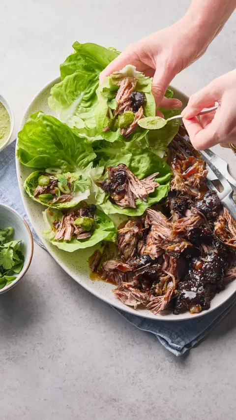 Slow cooked lamb is presented shredded in an oval dish and served with lettuce leaves.