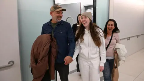 GPO Ab beaming Naama Levy holds hands with her father and mother by her side as they leave a facility in Israel in a picture released by Israeli authorities on 25 January 2025.