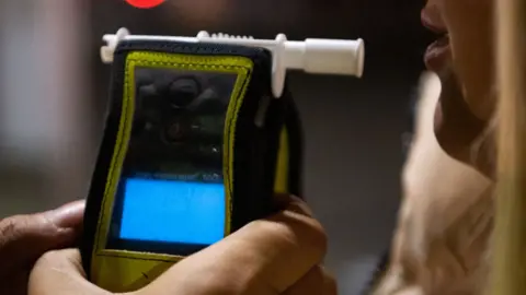 Generic close-up image of a breathalyser in a police officer's hand, in front of a woman's mouth