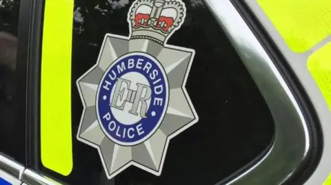 The Humberside Police logo with Humberside Police in a blue circle, ER in the middle and a star and crown around it. Located on the side of a police car