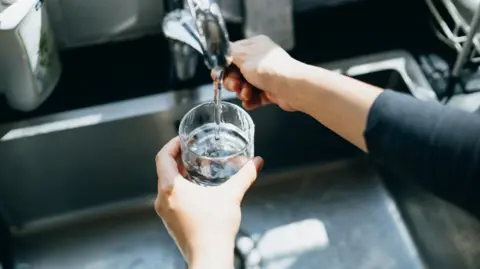 A glass being filled with water over a sink