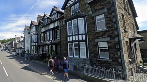 Devonshire House, a large old building, with Tudor panelling and is part of terraced housing in Rothay Road. People walk in the street.