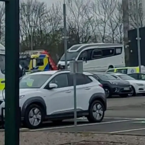 David Cardwell A white campervan in a compound. There us a white car in the foreground and other cars and police vehicles parked elsewhere.