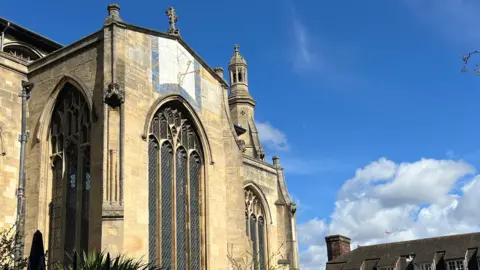 A blue bordered sundial with golden dials and Roman numerals on the side of the cream stone church displays the time in the sunshine.