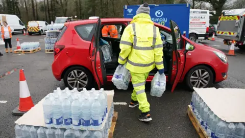 PA Media A worker carries bottled water to a car at a water station in East Grinstead, after bad weather was blamed for more water outages