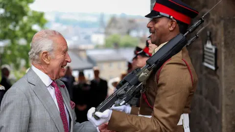 Reuters King Charles inspects the honour guard during the Ceremony of the Keys at Lancaster Castle. He is seen laughing with a soldier in a brown uniform holding a rifle on his shoulder