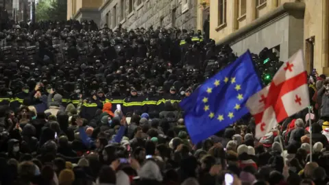 Reuters Supporters of Georgia's opposition attend a rally to protest after the government halted the EU application until 2028, as police officers block a street near the Parliament building, in Tbilisi