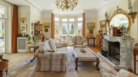 Savills A living room with white furnishings and white walls has a large marble fireplace on the right side with a gold rimmed mirror sat on top.