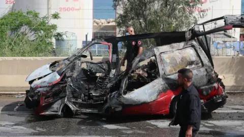 Lebanese rescuers and army soldiers inspect the wreckage of a vehicle that was hit in an Israeli strike in Jiyeh, south of Beirut, Lebanon (13 May 2026)