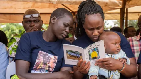 Los dolientes de la EPA leen el orden del servicio durante el funeral de la fallecida atleta olímpica ugandesa Rebecca Cheptegei, sargento de las Fuerzas de Defensa del Pueblo de Uganda, en el distrito de Bukwo, a unos 370 km al este de Kampala, Uganda, el 14 de septiembre de 2024