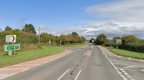 The A44 junction with the A4110 is in countryside with road signs and there are chevrons on the side of the 