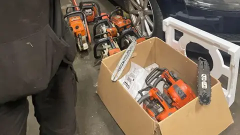 CPS The bottom half of Carruthers dressed in black next to a box of chainsaws