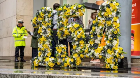 Transport for Greater Manchester The flower display is in the shape of the number 154. There is a range of colours including yellow and white flowers.