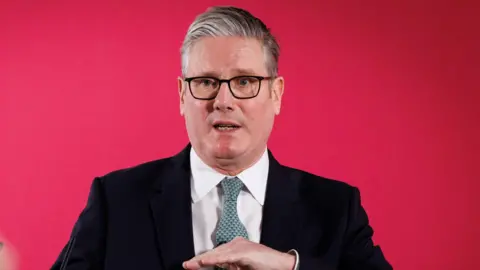 EPA British Prime Minister Keir Starmer delivers a speech in London on 1 December. He is wearing glasses, a black suit and a white shirt and tie. He is gesturing with his hands as he speaks.