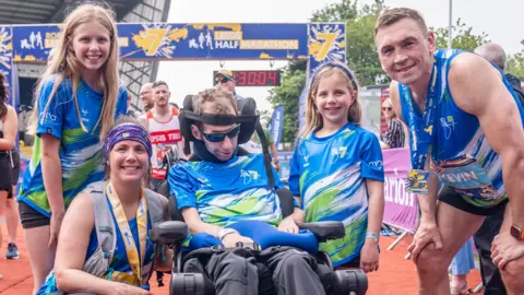 PA Media Rob Burrow alongside wife Lindsey (who ran the half marathon), daughters Macy and Maya and Kevin Sinfield who ran the full marathon all pose for a picture after the Rob Burrow Leeds Marathon in 2024.