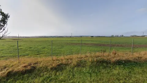 A view of a grass field with metal fence poles in the foreground
