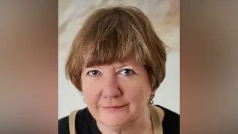 Sarah Milne Sarah Milne smiles at the camera. She has short brown hair, some of which rests over her forehead. She wears a black top and small earrings. 