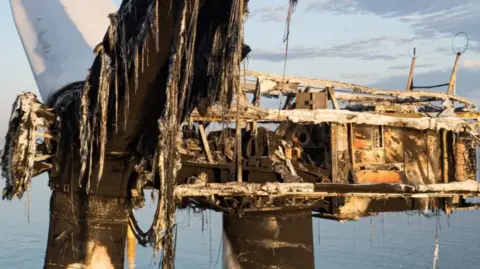 Olivers Drone Photography The image shows the burned remains of the turbine blades and gearbox housing. Molten plastic can be seen, with smoke and charring stains.