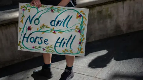 Getty Images A sign which reads No drill Horse Hill being held by an unseen person, it is decorated with pictures of flowers