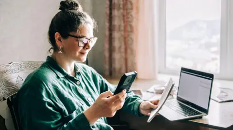 Woman looks at mobile and pad while working on a computer at home.