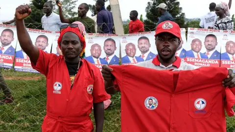 Getty Images Two supporters of Bobbi Wine, one in a red boiler suit, the other holding one up for the cameral pose for the camera. The one on the left, in the boiler suit, holds his fist in the air.